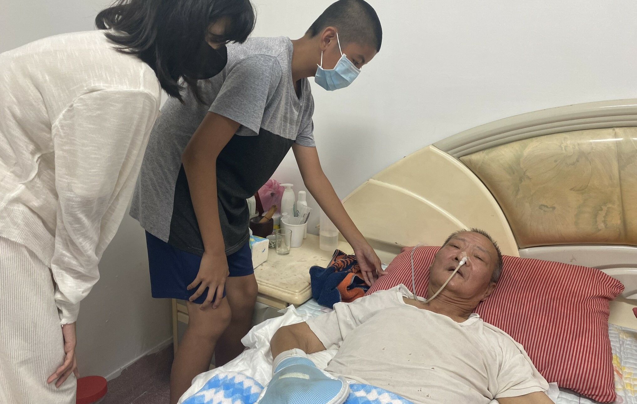 64歲阿奇伯（右）工作時從二樓高度重摔至今仍臥床，12歲孫子小鴻（中）與14歲孫女小馨（左）希望阿公快恢復健康。王雪玲攝