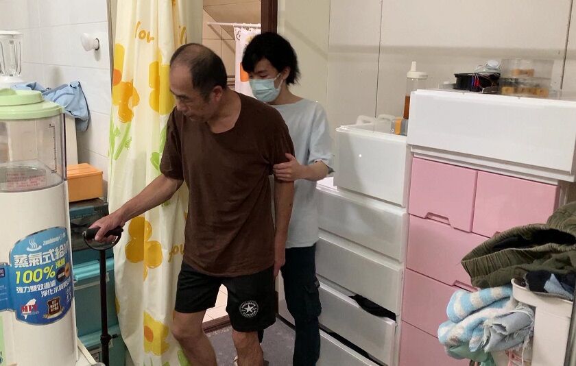 62歲的阿賢（左）中風左側偏癱無力，就讀大四的兒子阿原需攙扶他行走，並協力生活起居。張嘉恬攝